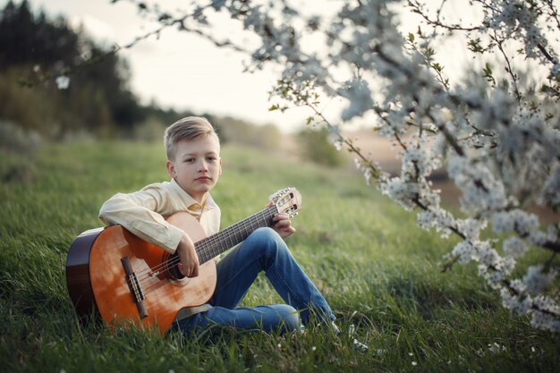 Garoto bonito fazendo música tocando guitarra na natureza.