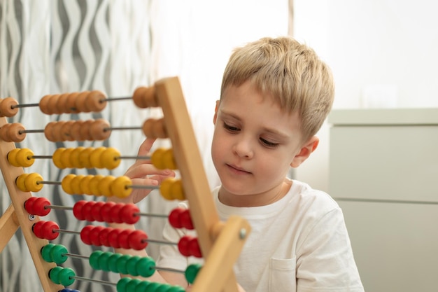 Garoto bonito loiro está envolvido com contas de madeira na mesa Jogos Montessori Educação conceitual