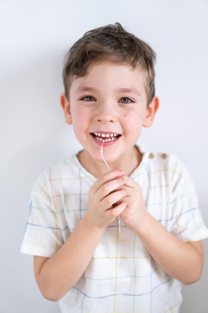 Garoto bonito puxando o dente solto usando um fio dental. Processo de remoção de um dente de leite.