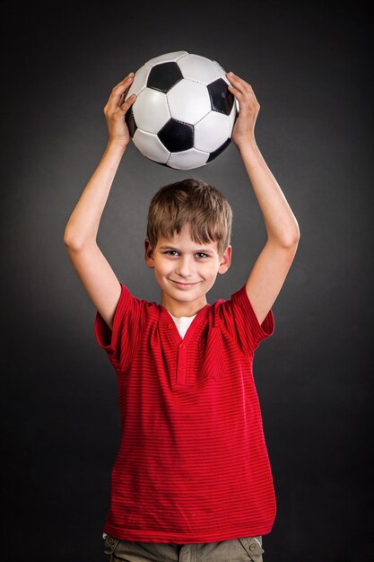 Foto garoto bonito segurando uma bola de futebol acima da cabeça