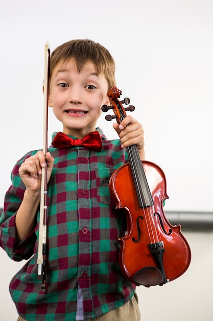 Garoto bonito segurando violino com laço na sala de aula