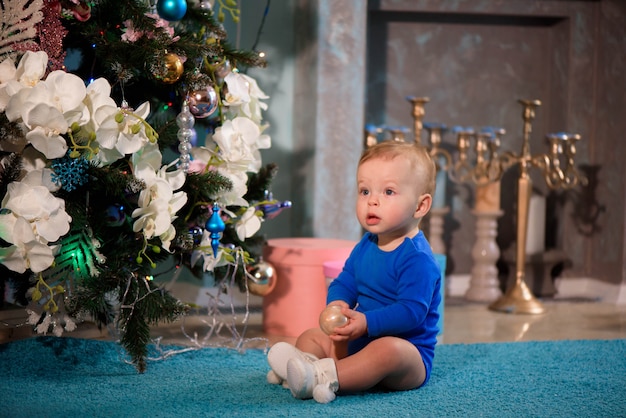 Garoto bonito sentado no tapete perto de árvore de natal