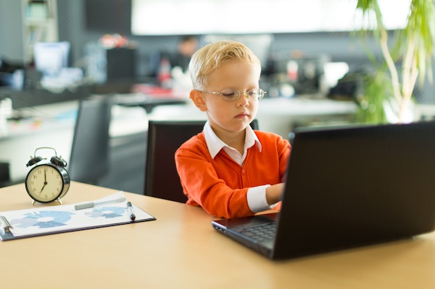 Garoto bonito sentar à mesa no escritório e usa o computador