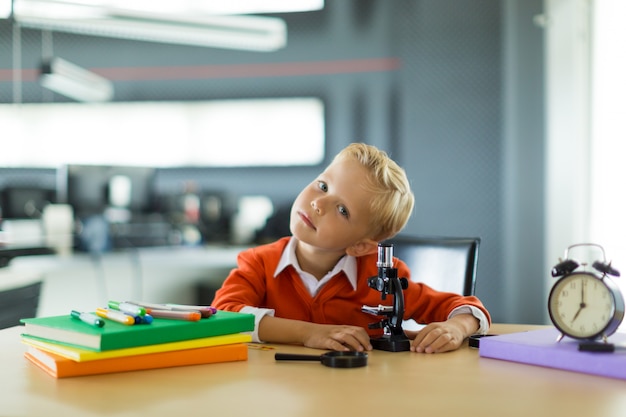 Garoto bonito sentar à mesa no escritório, segure o microscópio