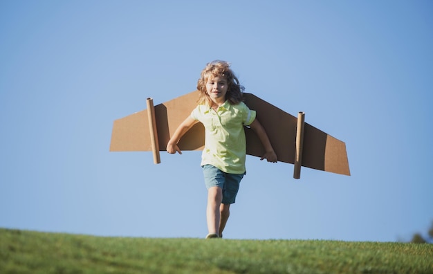 Garoto brincando com asas de papelão criança no campo de verão crianças viajam e conceito de férias imaginat