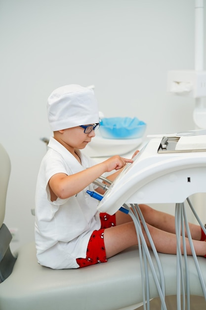 Garoto brincando com equipamentos odontológicos Garotinho de jaleco branco brincando no dentista