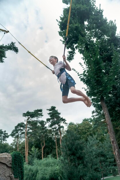 Garoto bungee jumping no trampolim Adolescente em um parque de diversões está se divertindo Quadro vertical