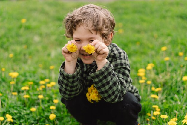 Garoto cacheado coleta e cheira flores de dente-de-leão