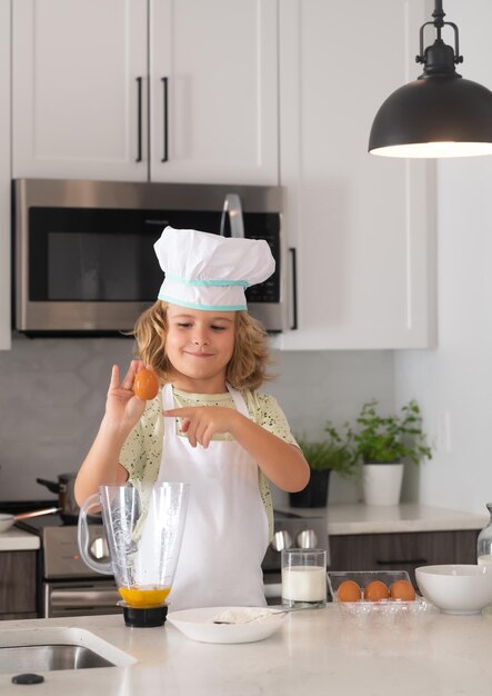 Garoto chef assando na cozinha Cozinheiro chef infantil prepara comida na cozinha Crianças cozinhando Garoto adolescente com avental e chapéu de chef preparando uma refeição saudável