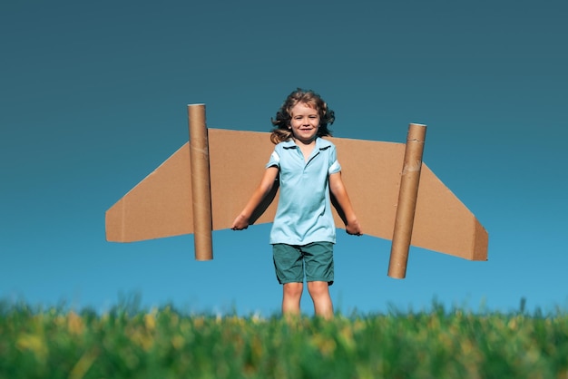 Garoto com brinquedo jetpack criança ao ar livre brincando no campo verde primavera com viagens de primavera de asas de papelão