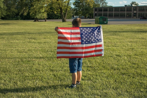 Garoto comemorando 4 de julho Dia da Independência dos EUA Criança correndo com o símbolo da bandeira americana dos Estados Unidos sobre o campo de trigo