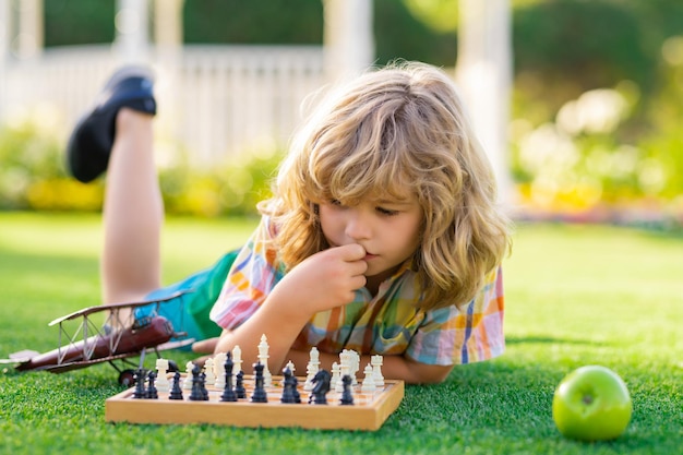 Garoto concentrado desenvolvendo estratégia de xadrez jogando jogo de tabuleiro no quintal deitado na grama