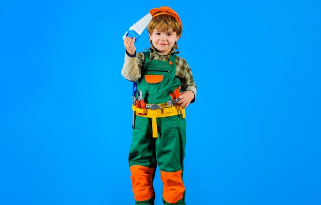 Garoto construtor em capacete de segurança e cinto de ferramentas com serra infantil em uniforme de construtor com ferramentas de cinto de ferramentas para