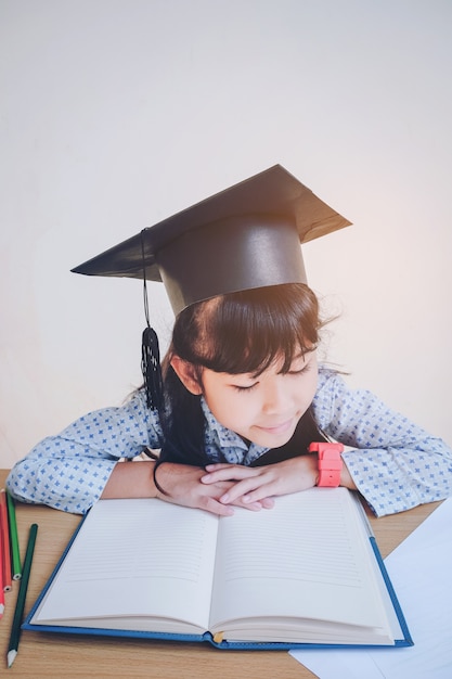 Garoto da escola asiática em boné de graduação e lendo um livro