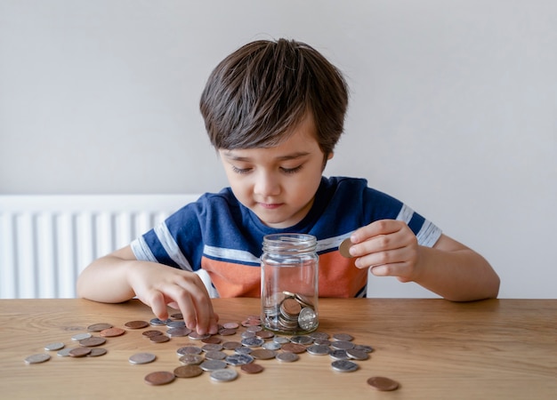 Garoto da escola colocando moedas em um frasco transparente, criança contando para economizar dinheiro