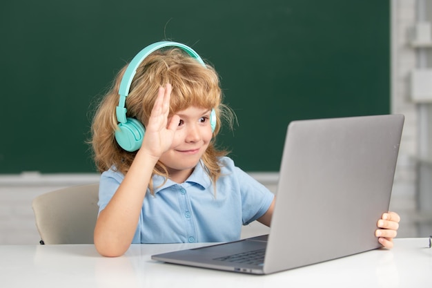 Garoto da escola inteligente, aluno fofo usa fones de ouvido escrevendo no laptop, ouve aula de áudio, usa vídeo de computador