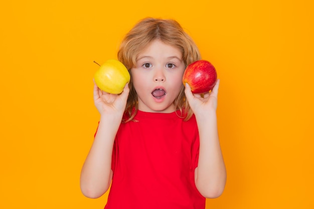 Garoto de camiseta vermelha com maçã no estúdio Retrato de estúdio de uma criança fofa segurando maçã isolada em fundo amarelo
