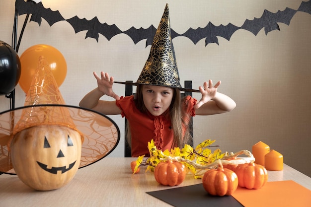 Garoto de chapéu preto se preparando para o Halloween em casa com abóbora jack-o-lanterna, velas, balões