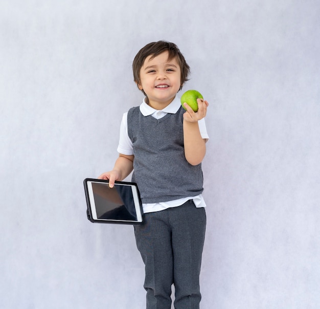 Garoto de escola segurando o tablet pc e maçã verde com um sorriso no rosto