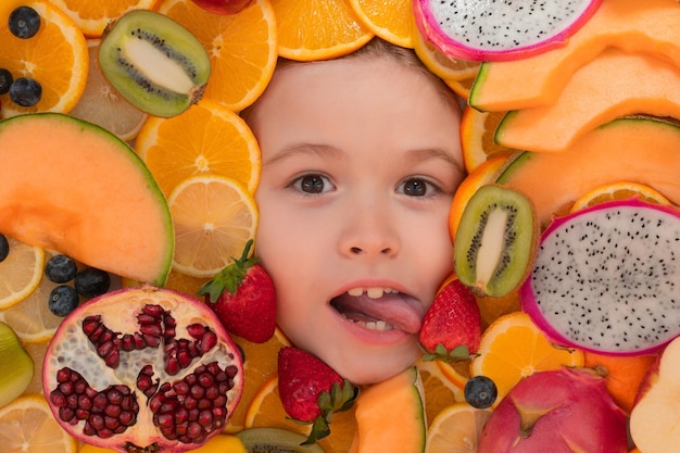 Garoto de fruta engraçado lambendo retrato de rosto sorridente cercado por frutas rosto de crianças está espreitando para fora