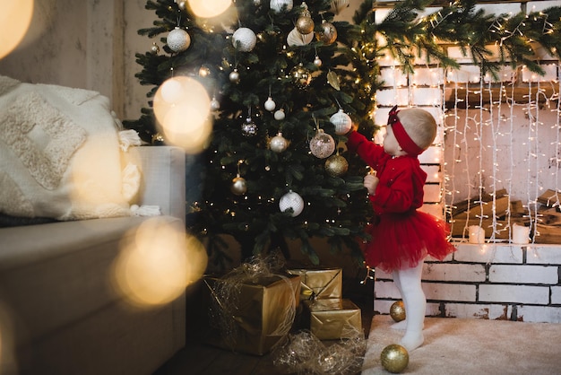 Garoto doce criança brincando com a árvore de natal na sala sobre luzes brilhantes