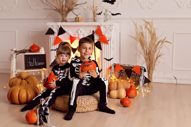 Foto garoto e garota engraçados com fantasia de esqueleto de halloween com jack de abóbora e vassoura dentro de casa