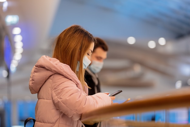 Garoto e garota mascarados estão usando o telefone celular no shopping da cidade em época de pandemia