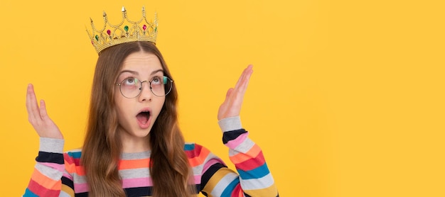 Garoto egoísta surpreso em óculos usa coroa de rainha em fundo amarelo Banner do retrato de inverno de garota de estúdio de criança de natal com espaço de cópia