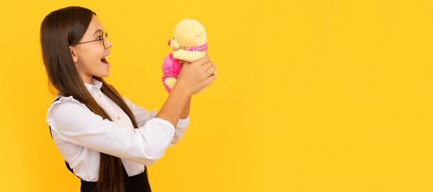 Foto garoto em idade escolar surpreso segura ursinho de pelúcia fundo amarelo presente de brinquedo banner de menina criança com cabeçalho de retrato de estúdio de brinquedo com espaço de cópia