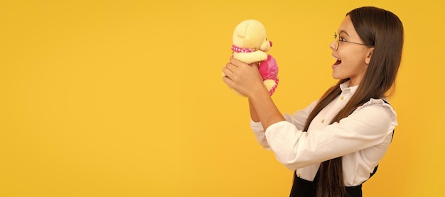 Garoto em idade escolar surpreso segura ursinho de pelúcia fundo amarelo presente de brinquedo Banner de menina criança com cabeçalho de retrato de estúdio de brinquedo com espaço de cópia