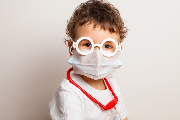 Foto garoto encaracolado engraçado em uma máscara médica e óculos. retrato maior de uma criança que exerce a profissão de médico.