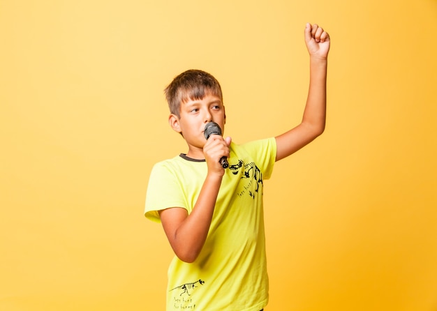 Foto garoto engraçado cantando com microfone em fundo amarelo