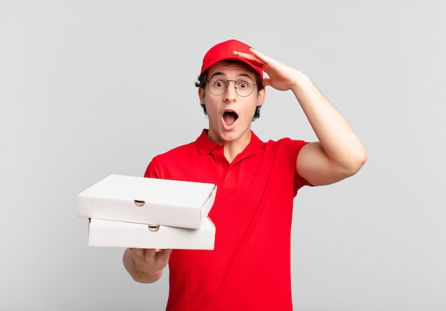 Garoto entregador de pizza parecendo feliz, surpreso e surpreso, sorrindo e percebendo uma boa notícia incrível