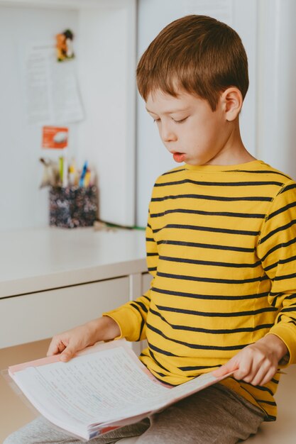 Garoto esperto usando óculos e lendo um livro em casa