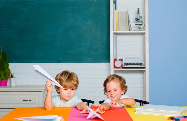 Garoto está aprendendo na aula no fundo do quadro-negro Aluno menino com expressão de rosto feliz perto da mesa com material escolar Aluno menino da escola primária no pátio da escola