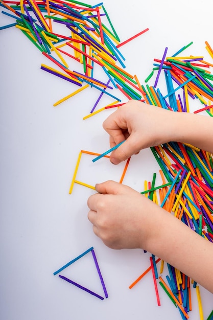 Garoto fazendo formas geométricas com palitos coloridos no fundo branco