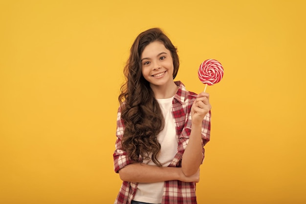 Garoto feliz com cabelo longo encaracolado segura doce de caramelo pirulito em fundo amarelo doce