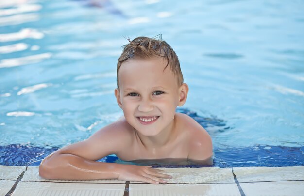 Garoto feliz com cabelos loiros sorrindo sentado na piscina