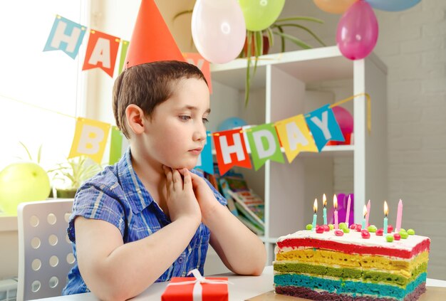 Garoto feliz com uma cara engraçada perto do bolo de aniversário. Festa de aniversario e bolo