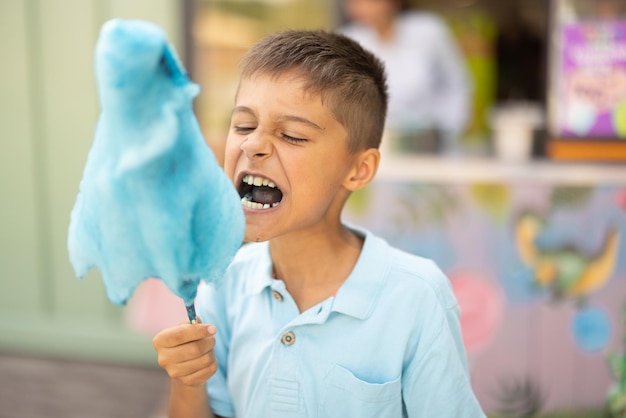 Garoto feliz come algodão doce azul enquanto visitava parque de diversões