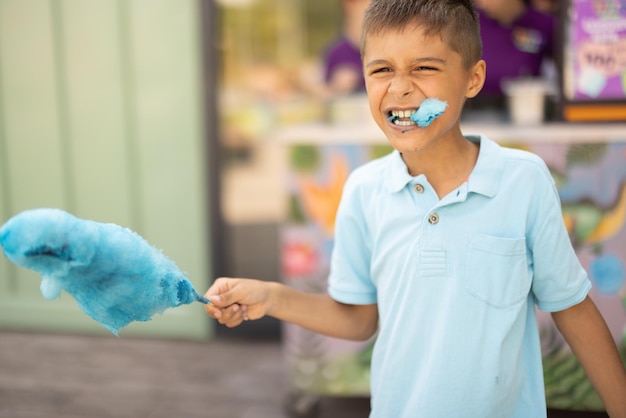 Garoto feliz come algodão doce azul enquanto visitava parque de diversões