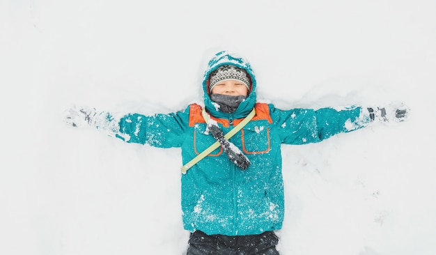 Garoto feliz, deitado na neve