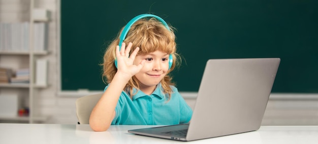 Garoto feliz em fones de ouvido assiste a vídeo aula no computador na escola em fones de ouvido tem menos online