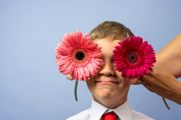 Garoto feliz em uma camisa branca fecha os olhos com flores gerbera vermelhas