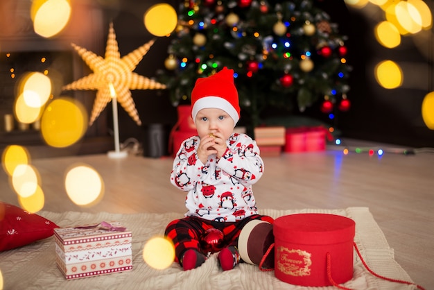 Garoto feliz, garoto com um chapéu de Papai Noel vermelho senta-se com decorações de Natal