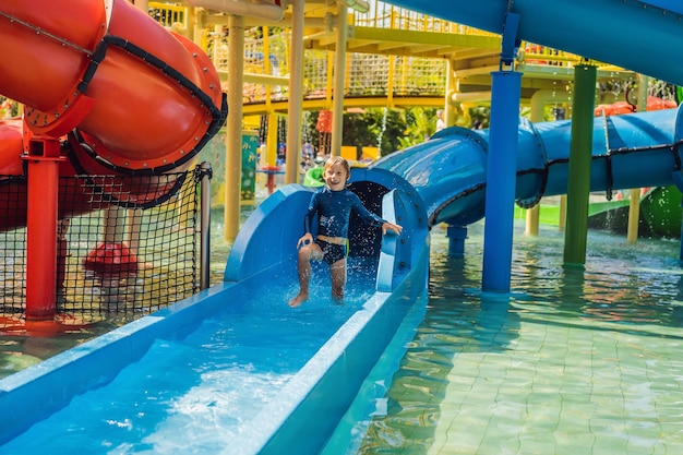 Garoto feliz no toboágua em uma piscina se divertindo durante as férias de verão em uma bela