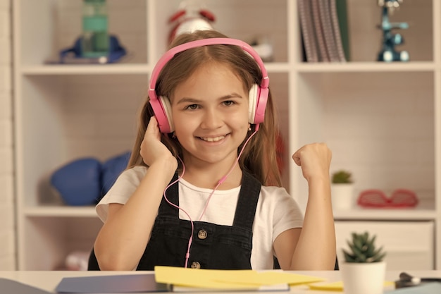 Garoto feliz ouve música em fones de ouvido na sala de aula da escola