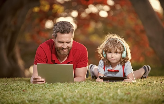 Garoto feliz ouve música em fones de ouvido webinar lição de vídeo educação on-line no laptop pai e filho usam tecnologia de comunicação sem fio no blog da família do parque infância e paternidade