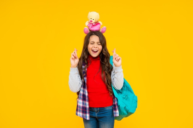 Garoto feliz tem cabelos longos e encaracolados, carrega mochila escolar segurando brinquedo na escola de fundo amarelo