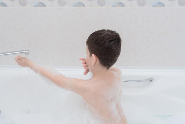 Garoto feliz toma banho com espuma exuberante brincando com bolhas Conceito de saúde de higiene pessoal